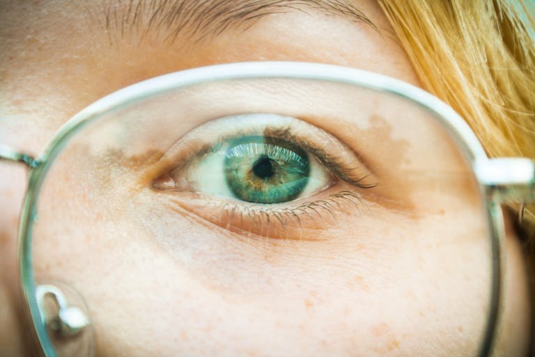 Detailed close-up of a person wearing glasses, highlighting blue eyes and blonde hair.
